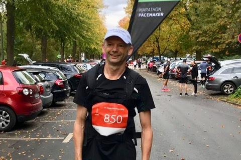 Mann in Sportkleidung steht mit einer Startnummer 850 und Pacemaker-Banner in einer parkenden Autoflut.