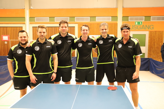 Sechs Tischtennisspieler in schwarzer Sportkleidung mit gr&uuml;nen Akzenten stehen vor einem Tischtennistisch.