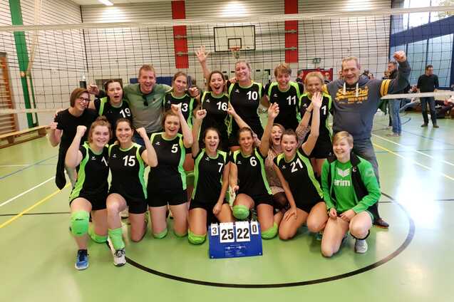 Gruppe von Volleyballspielern in gr&uuml;n-schwarzen Trikots feiert einen Sieg vor dem Netz, Punktestand 25:22.