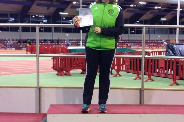 Sportlerin steht auf dem Siegertreppchen und h&auml;lt eine Urkunde in der Hand, Hintergrund einer Sporthalle.