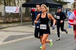 L&auml;uferinnen und L&auml;ufer absolvieren ein Stra&szlig;enrennen, w&auml;hrend im Hintergrund ein Zelt und Zuschauer zu sehen sind.