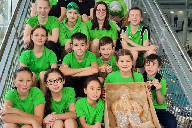 Gruppe von Schwimmern in gr&uuml;nen T-Shirts sitzt auf Treppe, eine Kiste mit Geb&auml;ck befindet sich im Vordergrund.