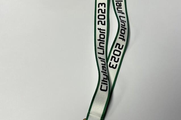 Holzmedaille mit gr&uuml;n-wei&szlig;em Band und Aufschrift &bdquo;Citylauf Linthorf 2023&ldquo; sowie Sportmotiven.