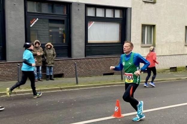 Ein L&auml;ufer mit Nummer 504 rennt auf einer Stra&szlig;e, w&auml;hrend Zuschauer im Hintergrund stehen.