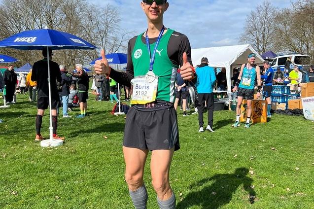 L&auml;ufer mit Startnummer 5192 posiert mit Daumen hoch auf einer Wiese, umgeben von Zuschauern und Veranstaltungspavillons.