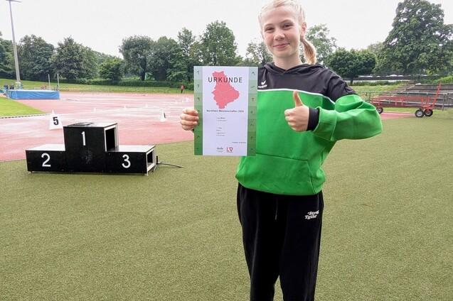 M&auml;dchen in Sportkleidung h&auml;lt stolz eine Urkunde und zeigt mit Daumen hoch, im Hintergrund eine Laufbahn und Podest.