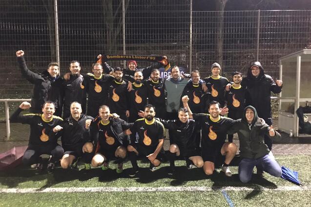 Mannschaft von Fu&szlig;ballspielern posiert in schwarzen Trikots mit Flammenlogo auf einem Kunstrasenplatz bei Nacht.