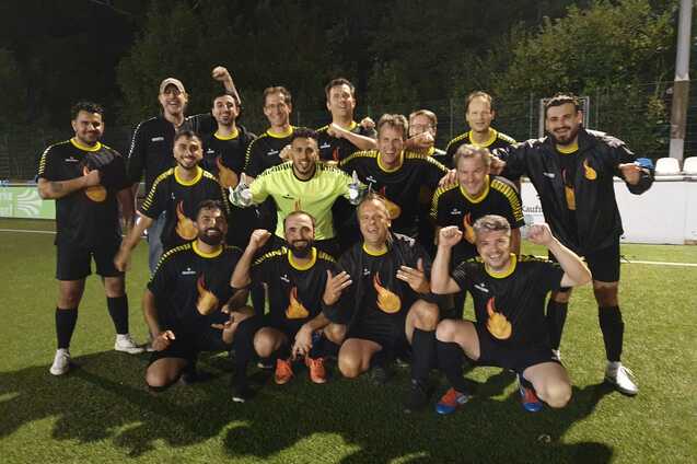 Gruppenfoto von zw&ouml;lf Fu&szlig;ballspielern in schwarzen Trikots mit gelben Details, posierend auf einem Kunstrasenplatz.