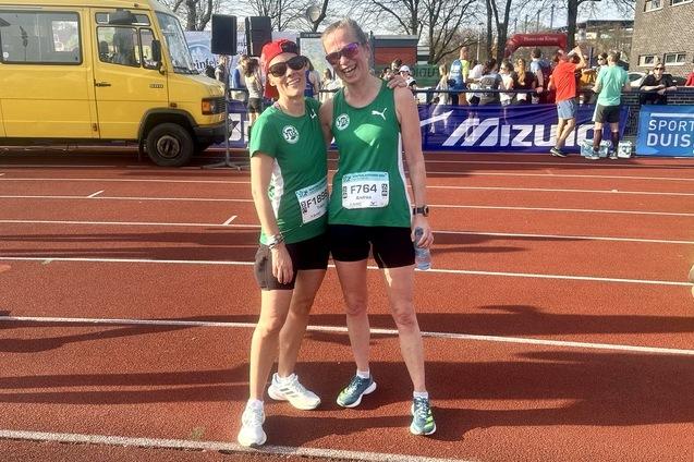 Zwei Frauen in Sportbekleidung stehen l&auml;chelnd nach einem Lauf auf einer Laufbahn, im Hintergrund ein gelbes Fahrzeug.