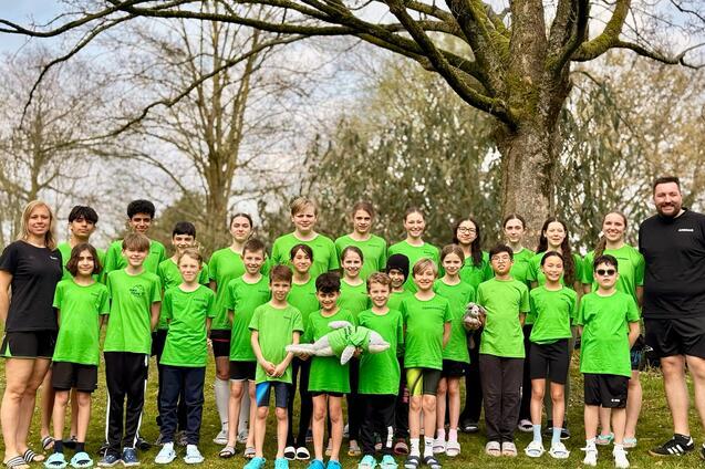 Gruppe von Jugendlichen und Trainern in gr&uuml;nen T-Shirts steht unter einem Baum auf einer Wiese.
