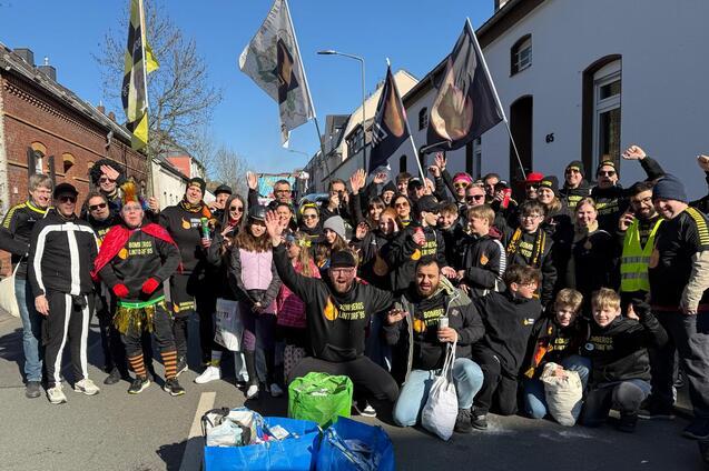 Gruppe von Menschen in Festkleidung, die auf einer Stra&szlig;e stehen und fr&ouml;hlich posieren, mit Flaggen im Hintergrund.