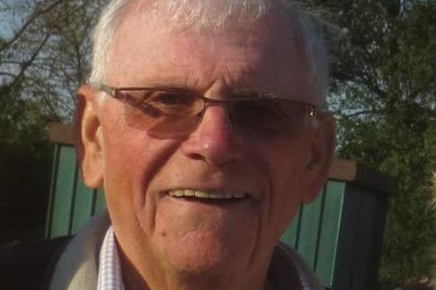 &Auml;lterer Mann mit Brille und l&auml;chelndem Gesicht, steht vor einer gr&uuml;nen Hintergrunwand aus Holz.