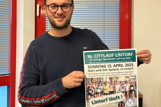 Mann h&auml;lt ein Plakat des 16. Citylauf Lintorf mit Details zum Event in einer B&uuml;roumgebung.