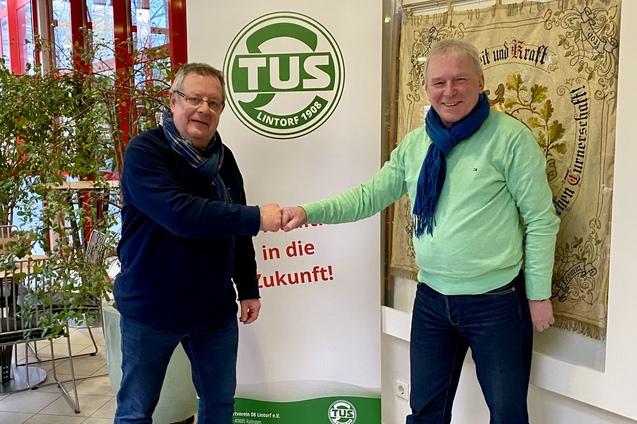 Zwei M&auml;nner sch&uuml;tteln sich die H&auml;nde vor einem Banner der TUS Lintorf in einem hellen Raum mit Pflanzen.