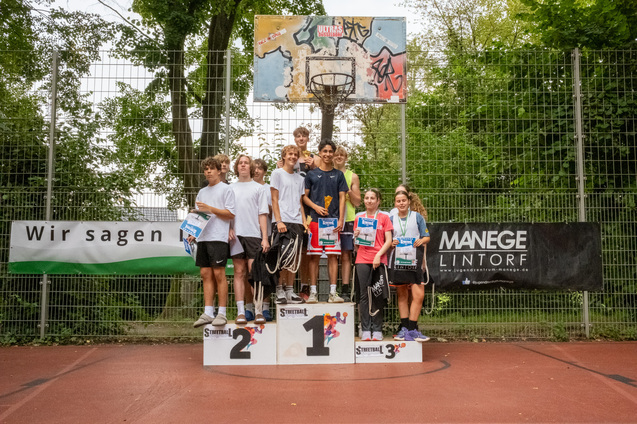 Gruppe von Jugendlichen steht auf dem Siegertreppchen nach einem Basketballturnier in einem Au&szlig;ensportbereich.