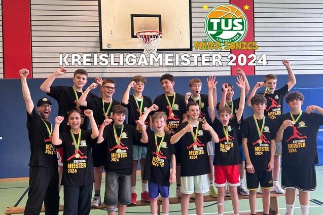 Gruppe von jugendlichen Basketballspielern in T-Shirts mit Medaillen, feiernd in einer Sporthalle nach dem Meisterschaftssieg.