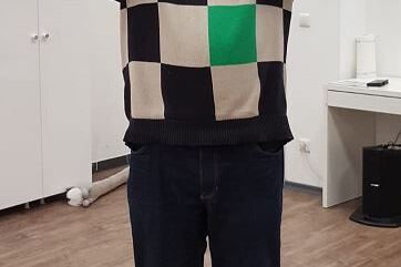 Mann mit buntem Pulli h&auml;lt einen Pokal &uuml;ber seinem Kopf in einem hellen Raum.