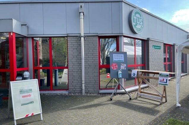 Eingangsbereich eines Sportvereins mit roten Fenstern, Hinweisschildern und einem Logo der Einrichtung.