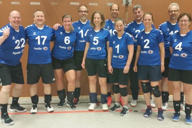 Mannschaftsfoto von zw&ouml;lf Handballspielern in blauen Trikots, l&auml;chelnd in einer Sporthalle aufgestellt.