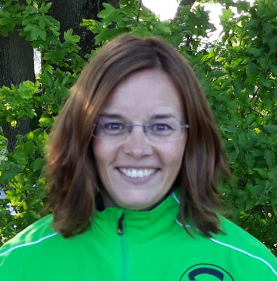 Frau mit Brille in gr&uuml;ner Sportjacke vor laubreiche Hintergrund.