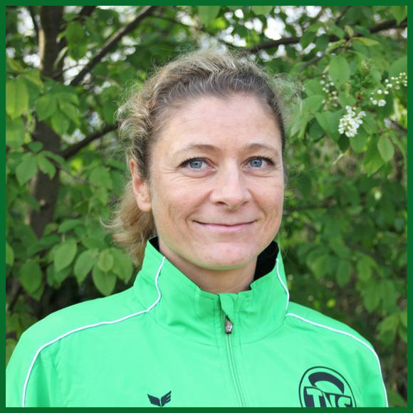 Portr&auml;t einer l&auml;chelnden Frau in gr&uuml;ner Sportjacke, vor einer gr&uuml;nen Pflanzenkulisse.