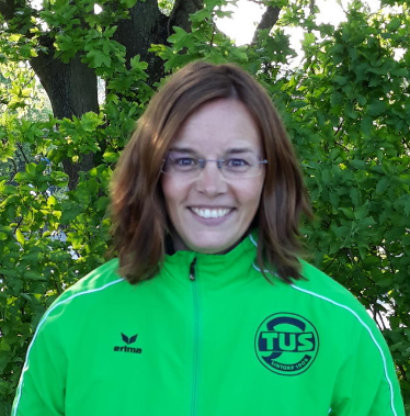 Frau mit Brille in gr&uuml;ner Sportjacke vor laubreiche Hintergrund.