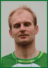 Portr&auml;t eines Mannes mit kurzer Frisur, der ein gr&uuml;nes Sporttrikot tr&auml;gt, mit neutralem Gesichtsausdruck auf hellem Hintergrund.