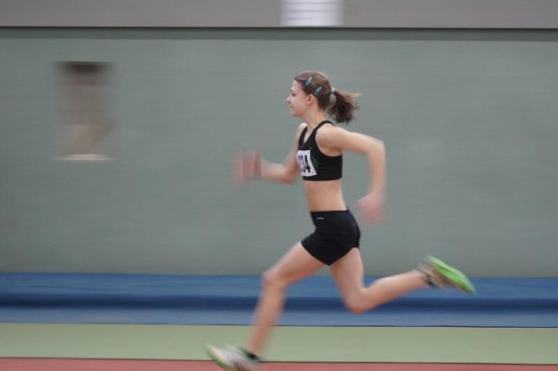 Läuferin in sportlicher Kleidung sprintet auf einer Laufbahn in einer Indoor-Arena.