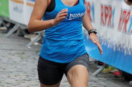 Frau in Sportkleidung l&auml;uft beim Wettlauf auf einer Pflasterstra&szlig;e, im Hintergrund Zuschauer und Werbebanner.