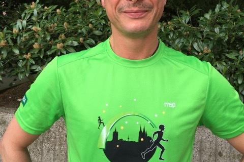 Sportler mit kurzem Haarschnitt tr&auml;gt ein gr&uuml;nes Laufshirt und eine Startnummer 160 vor einer bepflanzten Wand.