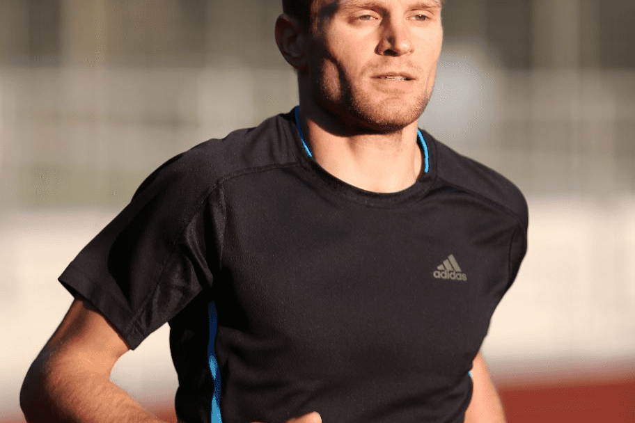 Mann in Sportkleidung l&auml;uft auf einer Laufbahn bei Sonnenlicht.