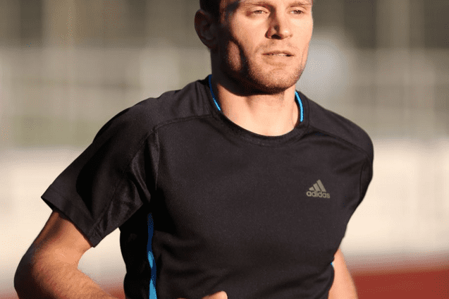 Mann in Sportkleidung l&auml;uft auf einer Laufbahn bei Sonnenlicht.