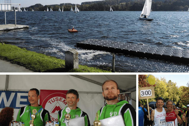 Drei M&auml;nner in Sportkleidung halten Pokale und Flaschen in einem Zelt, im Hintergrund eine Wettkampfbanner.