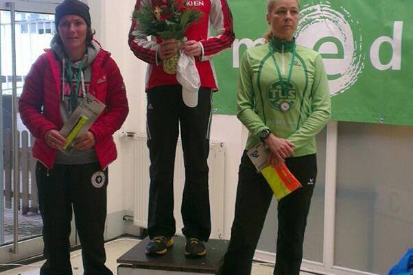 Drei Frauen stehen auf einem Siegertreppchen; die mittlere h&auml;lt einen Blumenstrau&szlig; und tr&auml;gt eine Medaille.