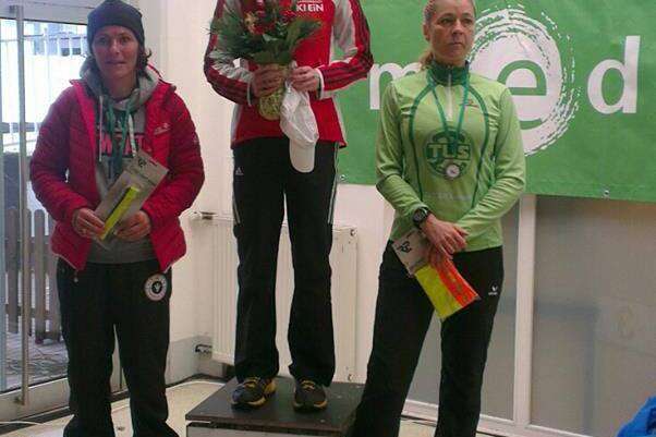 Drei Frauen stehen auf einem Siegertreppchen; die mittlere h&auml;lt einen Blumenstrau&szlig; und tr&auml;gt eine Medaille.