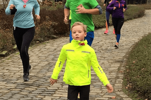 Gruppe von Joggern auf einem gepflasterten Weg, darunter ein Junge in neonfarbener Jacke, alle mit l&auml;chelnden Gesichtern.