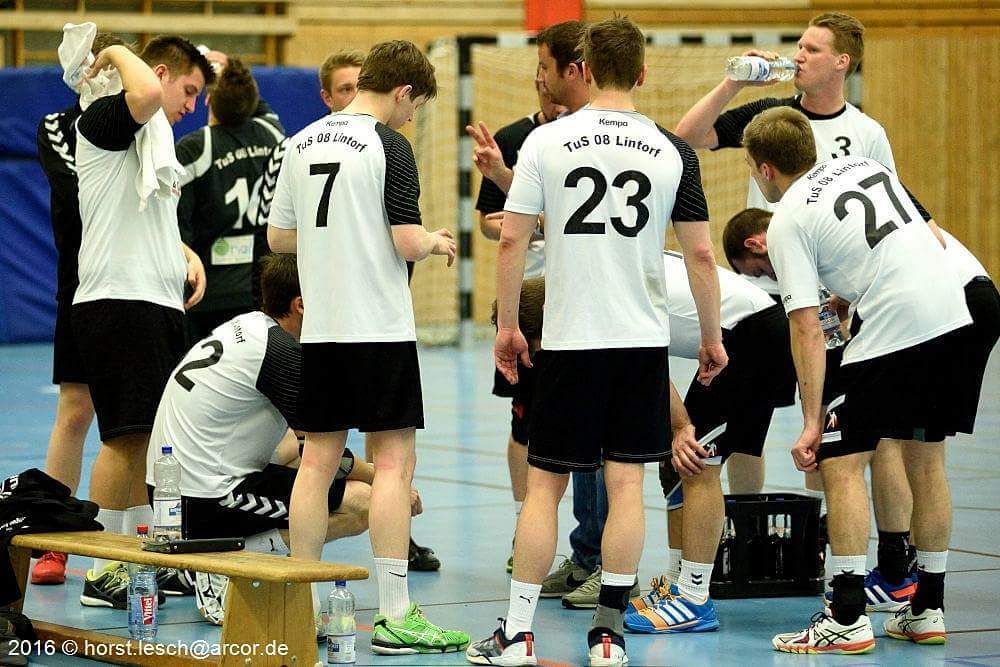 Gruppenszene eines Handballteams in Trikots w&auml;hrend einer Pause, einige Spieler trinken Wasser und diskutieren.