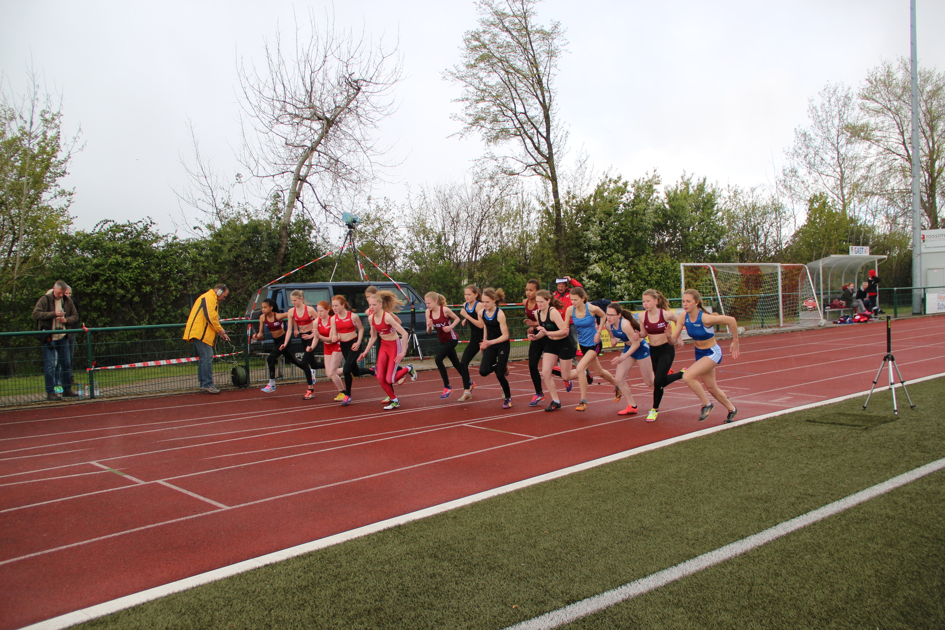 Start eines Frauenrennens auf einer roten Laufbahn, mit mehreren Athletinnen in Sportkleidung und Zuschauern im Hintergrund.