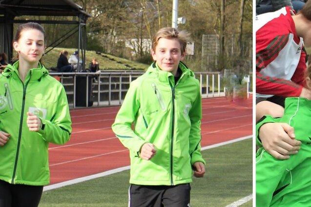 Drei Kinder in gr&uuml;nen Sportjacken joggen auf einer Laufbahn, w&auml;hrend zwei weitere Kinder sitzen und l&auml;cheln.