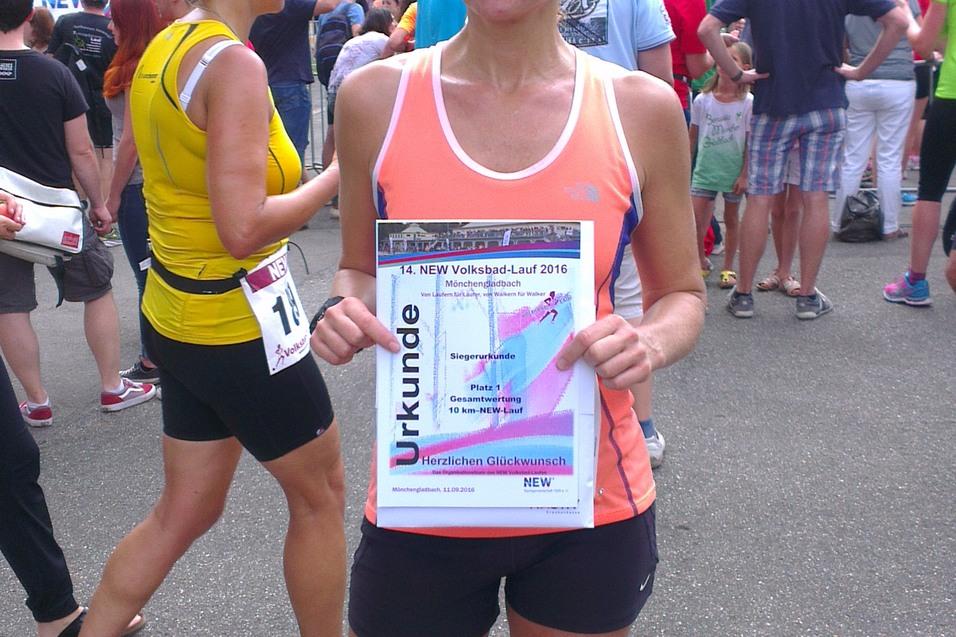 Frau mit Medaille und Urkunde steht vor einer Menschenmenge nach Volkslauf, umgeben von B&auml;umen und Verkaufsst&auml;nden.