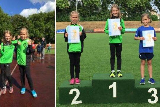 Zwei M&auml;dchen in gr&uuml;nen Trikots posieren auf einem Sportplatz, w&auml;hrend drei M&auml;dchen auf dem Siegertreppchen Urkunden halten.