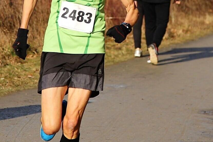 L&auml;ufer in gr&uuml;nem Trikot mit der Nummer 2483, der auf einem asphaltieren Weg unterwegs ist, umgeben von B&auml;umen.