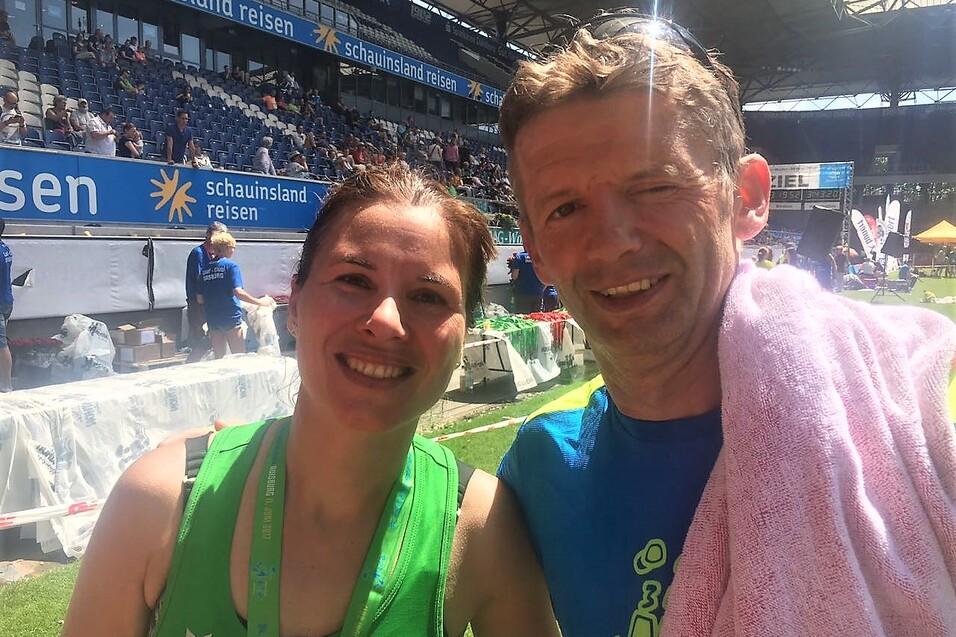 L&auml;chelndes Duo auf einem Sportevent, im Hintergrund St&auml;nde und Trib&uuml;nen in einem Stadion.