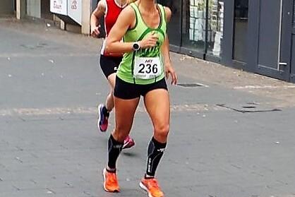 Zwei Läuferinnen in Sportbekleidung joggen auf einer Stadtstraße, eine vorne mit Startnummer 236 und grüner Tanktop.