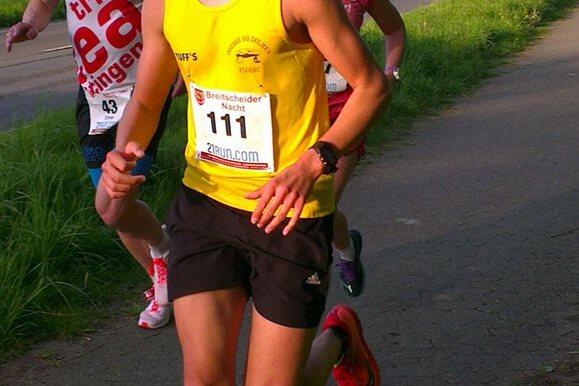 Drei L&auml;ufer nehmen an einem Stra&szlig;enlauf teil, einer im gelben Shirt mit Startnummer 111 vor zwei weiteren Teilnehmern.