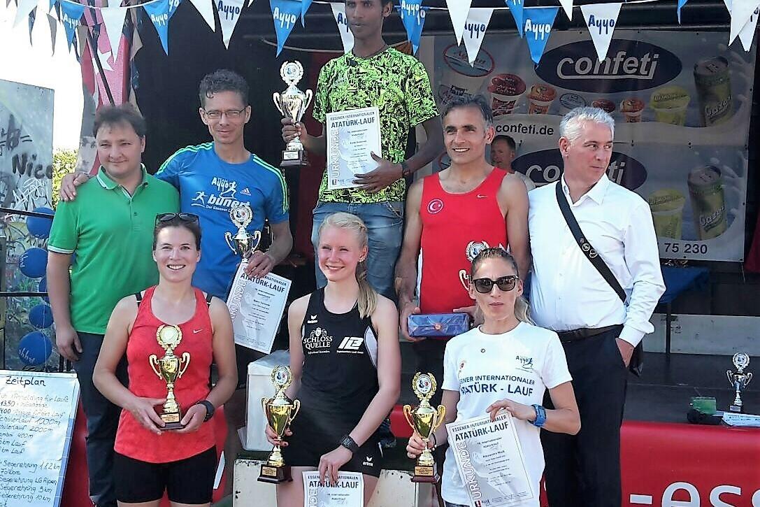 Sieben L&auml;uferinnen und L&auml;ufer stehen auf einer B&uuml;hne mit Pokalen und Urkunden nach einem Wettkampf.