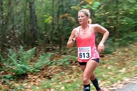 Läuferin in pinkem Shirt mit der Nummer 613 joggt auf einem Waldweg zwischen buntem Herbstlaub.