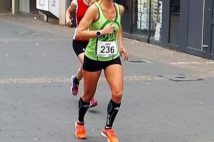 Zwei L&auml;uferinnen in Sportbekleidung joggen auf einer Stadtstra&szlig;e, eine vorne mit Startnummer 236 und gr&uuml;ner Tanktop.