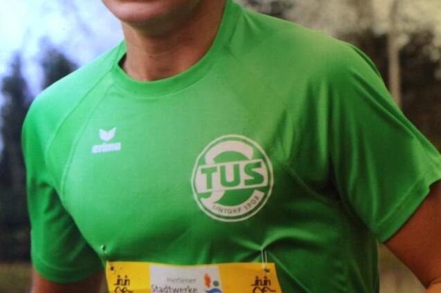 L&auml;ufer in gr&uuml;nem Shirt mit Startnummer 3260, beim Wettkampf auf einem Sportplatz mit B&auml;umen im Hintergrund.