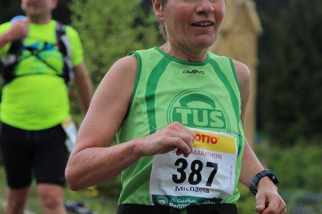 L&auml;uferin in gr&uuml;nem Trikot mit Startnummer 387 joggt auf einem Weg, im Hintergrund ist eine Kirche und Natur zu sehen.